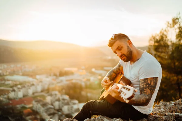 Young guitarist playing acoustic guitar and looking to sunset.Searching inspiration.Music creator.New artist.Musical talent.Handsome guitarist enjoying sunset and playing acoustic guitar.