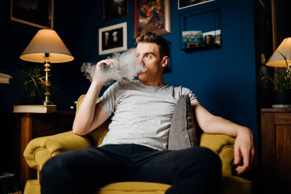 Young man inhaling of a vapor with electronic cigarette.Vape flavor liquid chemicals.Parent use of e-cigarettes in the home.Smoking and vaping negative health effects.Smoking habit,nicotine addiction.