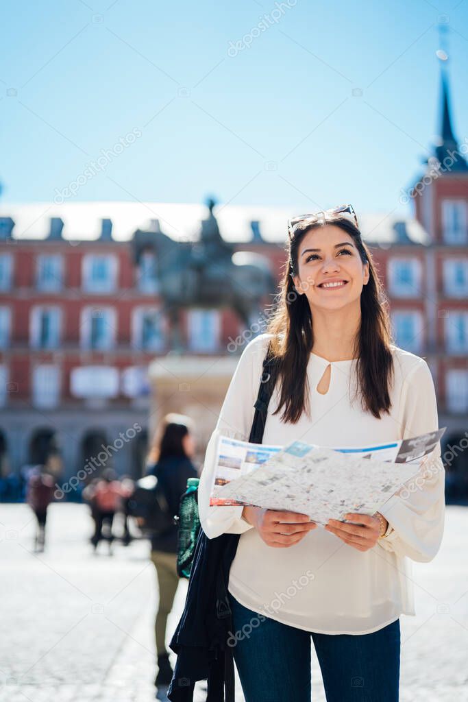 Young happy woman exploring center  of Madrid. visiting famous landmarks and places.Cheerful female traveler at famous Plaza Mayor square admiring statue of Philip III.Spain travel experience.