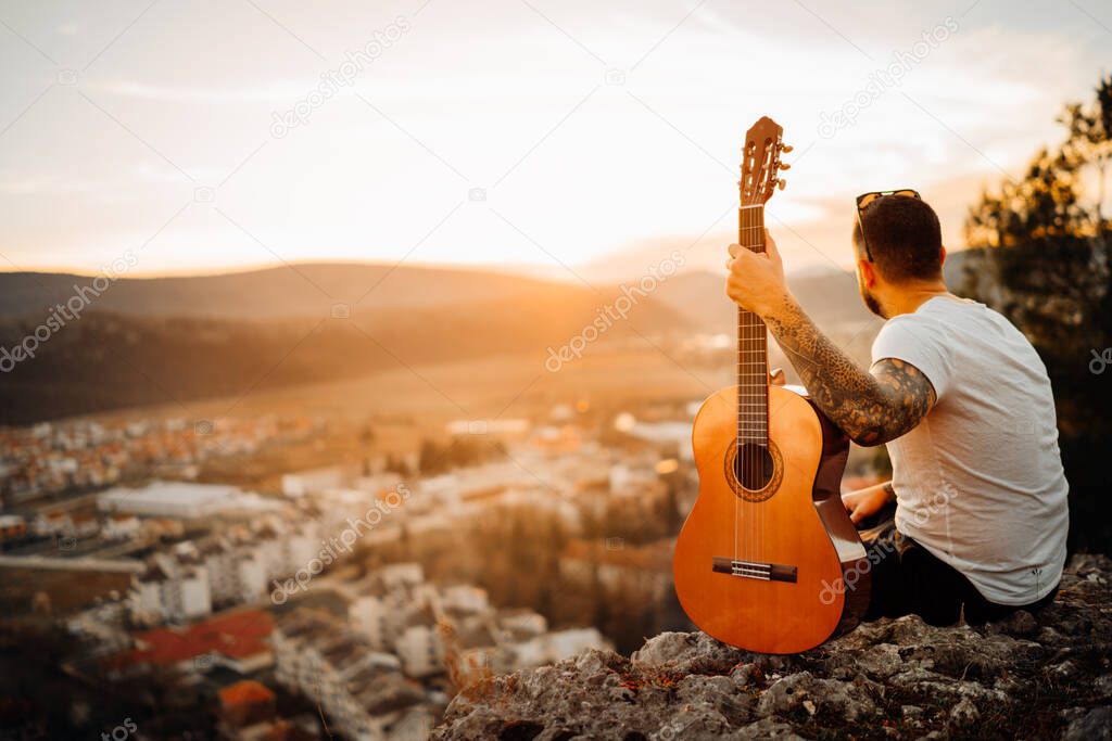 Young man holding acoustic guitar and looking to sunset.Searching inspiration.Music creator.New artist.Musical talent.Handsome guitarist enjoying sunset and playing acoustic guitar.