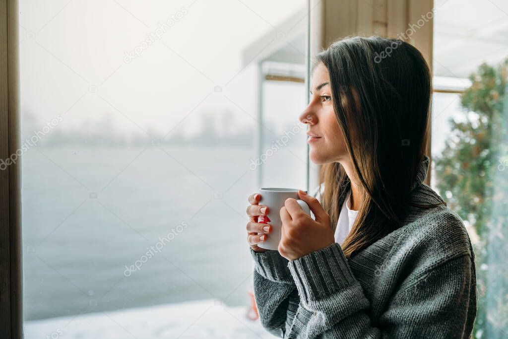 Young woman spending free time home.Self care,staying home.Enjoying view,gazing through to the window.Quarantined person indoors.Serene mornings.
