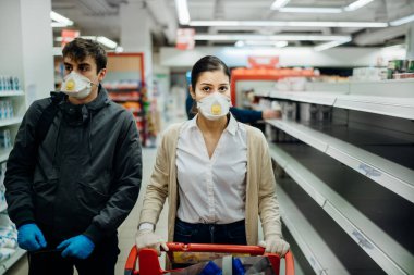 Maske takan ve eldiven giyen bir çift, marketten tükenmiş ürünlerle erzak / erzak alıyor. Coronavirus covid-19 salgını nedeniyle yiyecek stokları azaldı..