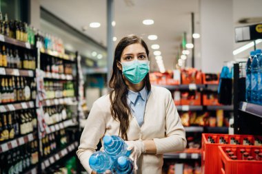 Koronavirüs salgınının ortasında marketten alışveriş yapan maskeli bir kadın. COVID-19 gıda alışverişi. Panik satın alma, stoklama. Su kıtlığı.