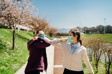 Two friends with protective masks greet with elbows.Elbow bump alternative greeting during quarantine to avoid physical contact.Coronavirus COVID-19 disease protection.Social distancing practice clipart