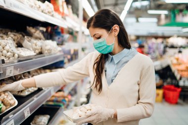 Koronavirüs salgınının ortasında marketten alışveriş yapan maskeli bir kadın. COVID-19 gıda alışverişi. Panik satın alma, stoklama. Taze ürün kıtlığı, sebze kıtlığı.