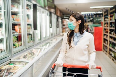 Maskeli bir müşteri markette Coronavirüs salgını nedeniyle market alışverişi yapıyor. COVID-19 alışverişi. Karantina hazırlığı. Panik satın alma ve stoklama. Süpermarkette kilitlenme tedbirleri.