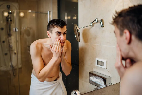 Young man having a shaving daily beard grooming routine,applying aftershave lotion.Allergic itchy rash burn reaction to hygiene skin care product.Facial hair removal.Shaving for work.Beard trim shave