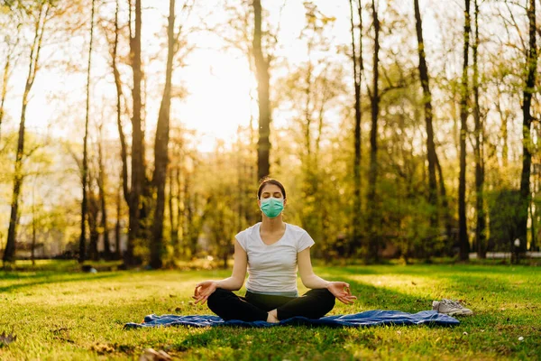 Woman with mask meditating in nature alone.Social distancing and active healthy lifestyle. Mindfulness meditation practice.Breathing exercise.Lotus yoga pose.Positive energy,optimism.
