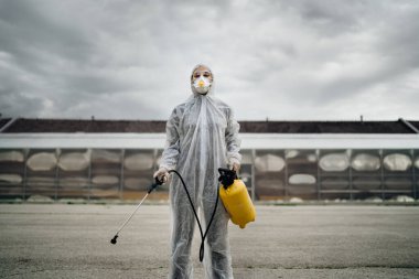 Tehlikeli madde koruma giysisi ve kimyasal dezenfekte spreyli N95 maskeli temizlik işçisi. COVID-19 yayılmasını önlemek için sokakları ve kamusal alanları dezenfekte ediyor. Coronavirüs dezenfeksiyon kavramı.