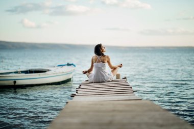Genç bir kadın sahilde tek başına oturuyor. Doğada karantina altında. Coronavirus karantina plaj gezisi. Sahile gidiyoruz. Açık hava aktiviteleri.