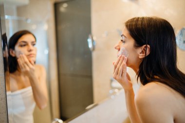 Genç bir kadın evde hidrasyon ürünleri, cilt rutini yayıyor. Gündüz yüz kremi. Makyaj çıkarılıyor. Spa günü, eğleniyor..