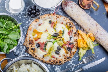 Kara tahta üzerinde mozzarella, salam, ricotta ve kabak çiçekleri ile geleneksel İtalyan pizza