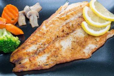 Siyah bir tabakta sebze ile ızgara balık yakın çekim