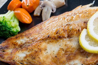 Siyah bir tabakta sebze ile ızgara balık yakın çekim