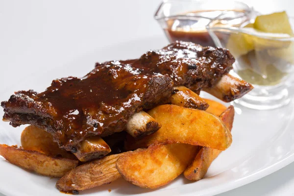 Sabrosas costillas de cerdo con salsa y pepinos en un plato — Foto de Stock