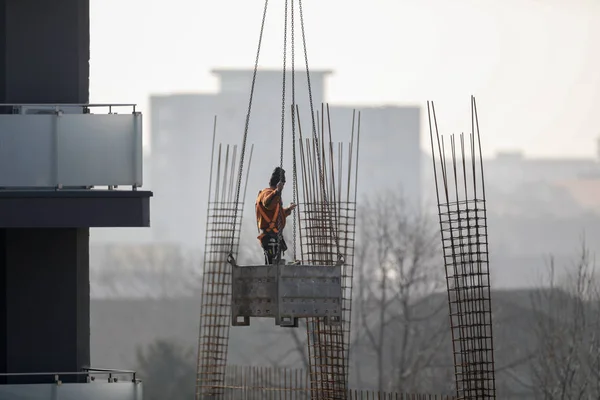man lifted with a crane on a construction site with a cityscape in background
