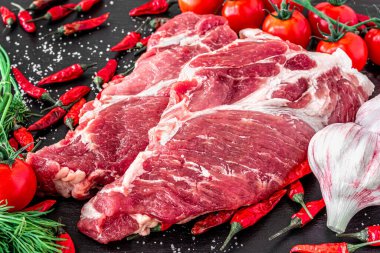 Çiğ, pişmemiş biftek New York 'ta, üzerinde domatesler ve biberiyeler olan, yatay görünümlü, taş bir tahtanın üzerinde.