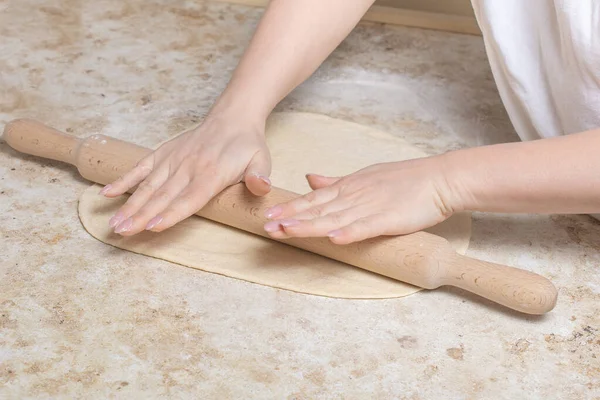 Closeup image of young woman rolling dough with wooden rolling pin. Housewife making pizza at home on kitchen. Bakery, nutrition. Making a pizza at home with tomato and cheese. quarantine