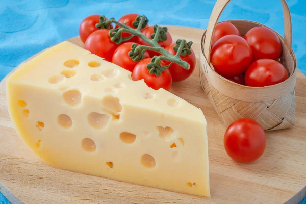 木の板の上のチーズ三角形のチーズ トマトの入ったバスケット 青いナプキンの背景 — ストック写真