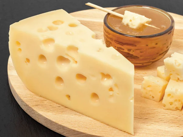 黄色のマダムチーズ 穴のある三角形のピースチーズ 蜂蜜とソーサー 黒の暗い石スレートの背景 — ストック写真