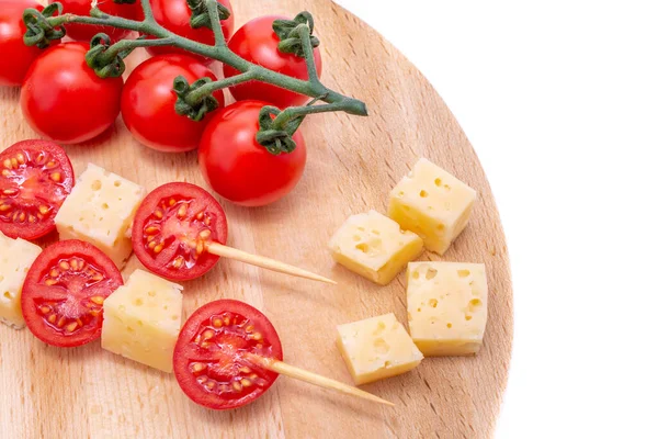 piece of cheese and cheese skewers with tomato on a wooden board, cheese samples, cheese with holes cutout on white background