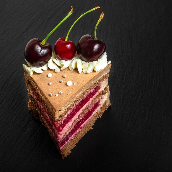 Detail on a Slice of a Black forest cake, or traditional austria schwarzwald cake from dark chocolate and sour cherries on black table