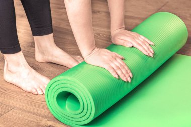 Ahşap zemindeki eğitimden sonra bir kadın yoga minderini yuvarlıyor. Yoga için ekipman. Sağlıklı yaşam tarzı, spor ve diyet kavramları.