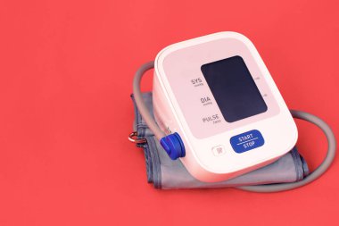 Tıbbi elektronik tonometre. Kırmızı tıbbi arka planda kan basıncı monitörü. Tıbbi konsept. Metin için boşluk.