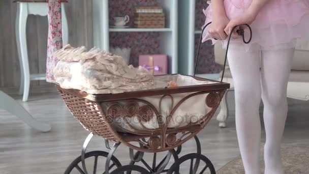 Menina está brincando em casa com uma boneca e está rolando-a em um carrinho — Vídeo de Stock
