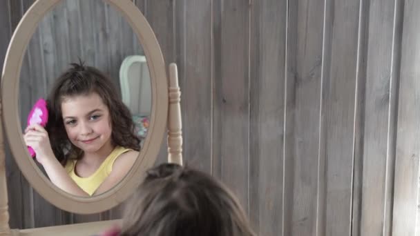 Liten flicka gör smink och frisyr som sitter framför en spegel — Stockvideo