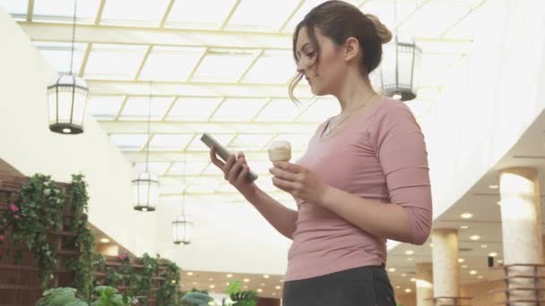 Mujer joven atractiva utiliza un teléfono inteligente y se come un helado — Vídeos de Stock