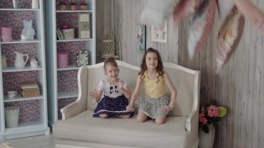 kanepe ve yastık atma üzerinde oturan kız. kanepede oturan oynarken küçük kız kız kardeş. ağır çekim