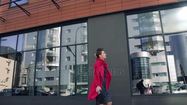 Donna sicura di sé con una bella insolita hairdress passeggiate attraverso la città primaverile. Ragazza sullo sfondo dell'architettura moderna. SLOW MOTION — Video Stock