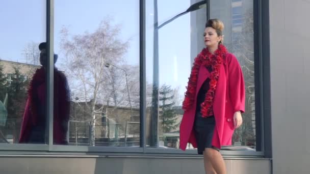 Schöne Mädchen in einem purpurfarbenen Mantel mit hellem Make-up und ungewöhnlicher Frisur geht durch die Stadt. Zeitlupe — Stockvideo