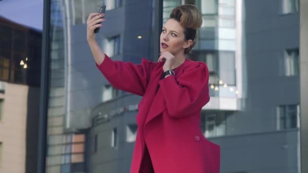 Confident woman with a beautiful unusual hairdress doing selfie spring city. Girl on the background of modern architecture. SLOW MOTION — Stock Video