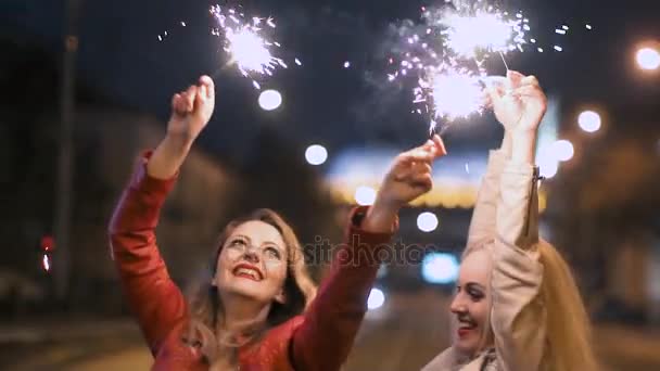 Mejores amigas se divierten juntas en la ciudad de la noche, sosteniendo en sus manos un chispeante fuegos artificiales en cámara lenta — Vídeo de stock