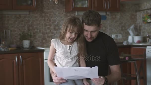 Apja egy magányos időt tölt a lányával, kislány az atyák ölében ül, és megmutatja neki a gyermek rajzok. lassú mozgás — Stock videók