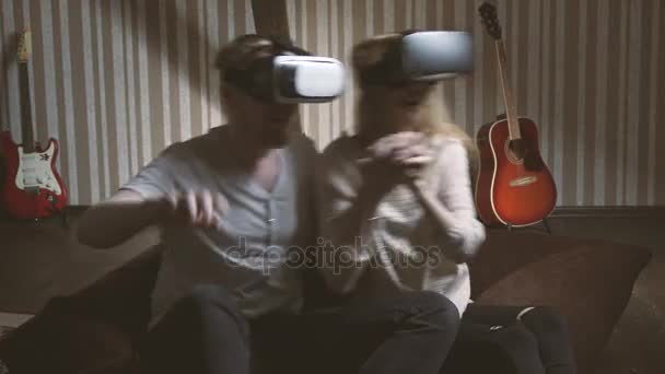 Spel via virtual reality-glasögon. en ung man och en attraktiv tjej som aktivt spelar i virtuell verklighet hjälmen — Stockvideo