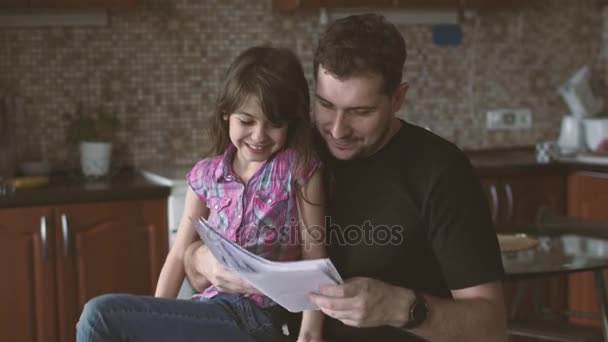 La niña le muestra sus dibujos a su padre. Padre e hija juntos — Vídeos de Stock