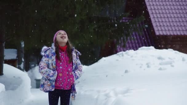 Portret van een meisje. Het kind geniet van de eerste sneeuw en sneeuwvlokken met zijn tong vangsten. Slow motion — Stockvideo