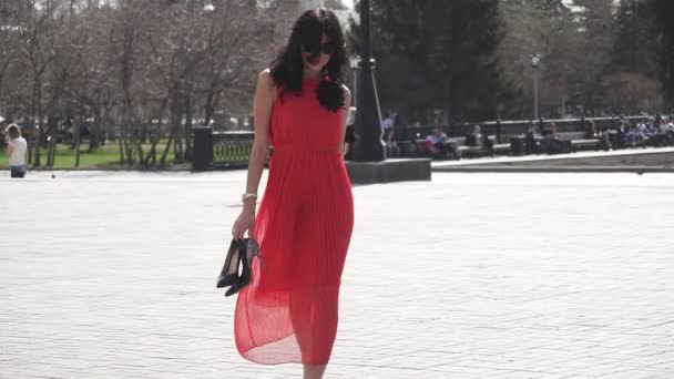 Sexy Mädchen in rotem Kleid und Sonnenbrille, die barfuß durch die Stadt laufen. Zeitlupe — Stockvideo