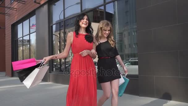 Chicas lindas se divierten caminando en la calle sosteniendo bolsas de compras. Los amigos pasan tiempo juntos. MOCIÓN LENTA — Vídeo de stock