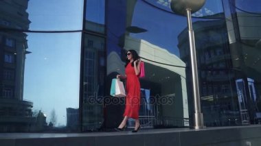 Kırmızı elbiseli çekici genç kız elinde çanta alışveriş ile eğleniyor. esmer yaz şehirde yürüyüş. Ağır çekim