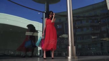 Güzel genç model şakacı kameraya bak. Küçük resmi güneş gözlüğü reklam ve alışveriş için uygundur. Kız storefronts yürüyüş. Ağır çekim