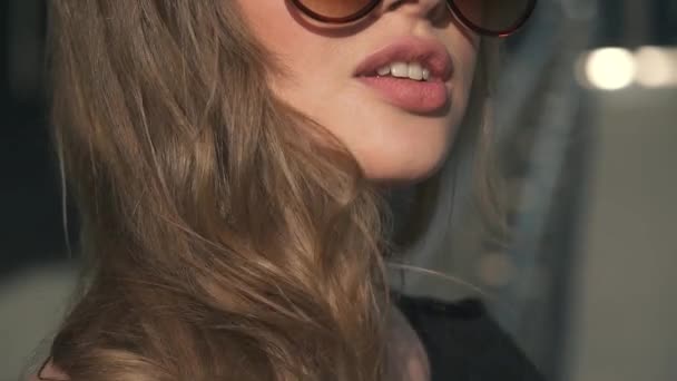 Close-up πορτρέτο της ένα γοητευτικό κορίτσι με όμορφα σέξι χείλη. Ξανθιά σε γυαλιά ηλίου ποζάρει στην κάμερα. αργή κίνηση — Αρχείο Βίντεο