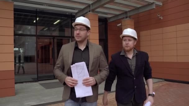 Двое архитекторов носят строительные шлемы. Инженеры держат план здания. Медленное движение — стоковое видео