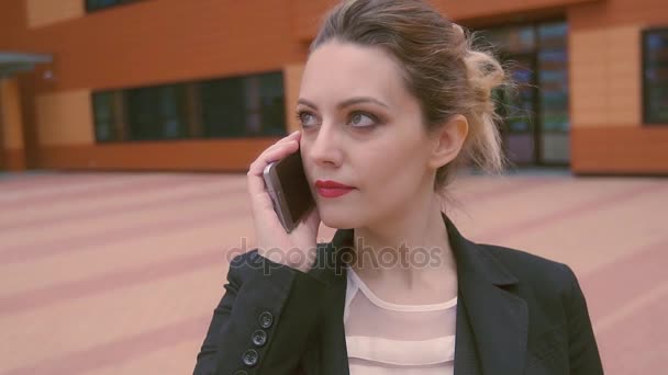 Atrakcyjny biznes młoda kobieta mówi przez telefon komórkowy. Aparat porusza się z modelem. zwolnionym tempie — Wideo stockowe