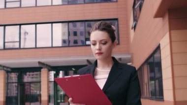 Bir iş kadını kendine güvenen bir yürüyüş ile hızlı bir şekilde yürür. Elinde kağıtlar için bir klasör. Kız bir iş toplantısı için geç oldu