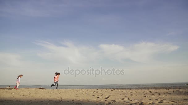 Τα παιδιά τρέχουν κατά μήκος στην άμμο στην παραλία. Δύο μικρά κορίτσια παίζουν στη θάλασσα. νωρίς την άνοιξη. αργή κίνηση — Αρχείο Βίντεο