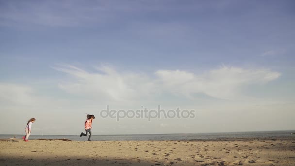 I bambini corrono lungo la sabbia sulla spiaggia. Due bambine stanno giocando al mare. inizio primavera. rallentatore — Video Stock